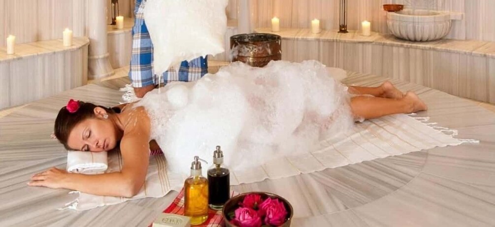 A person lying on a white, fluffy surface in a spa setting with candles and bottles of essential oils. 1