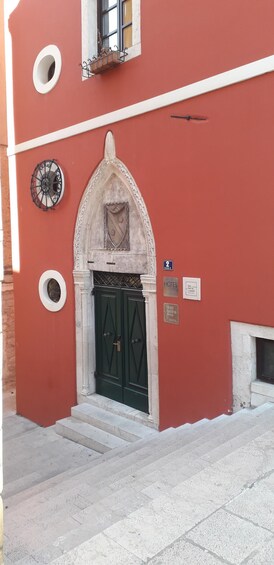 A red building with a green door, a small balcony, and a circular window. 2