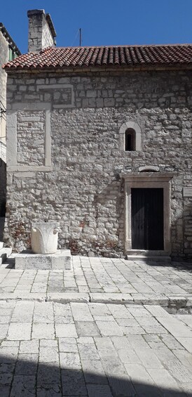 A stone building with a tiled roof, a large arched window, and a door. 3