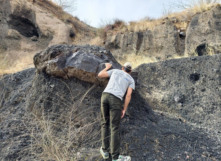 A person examining a large rock formation in a dry, rocky landscape. 5