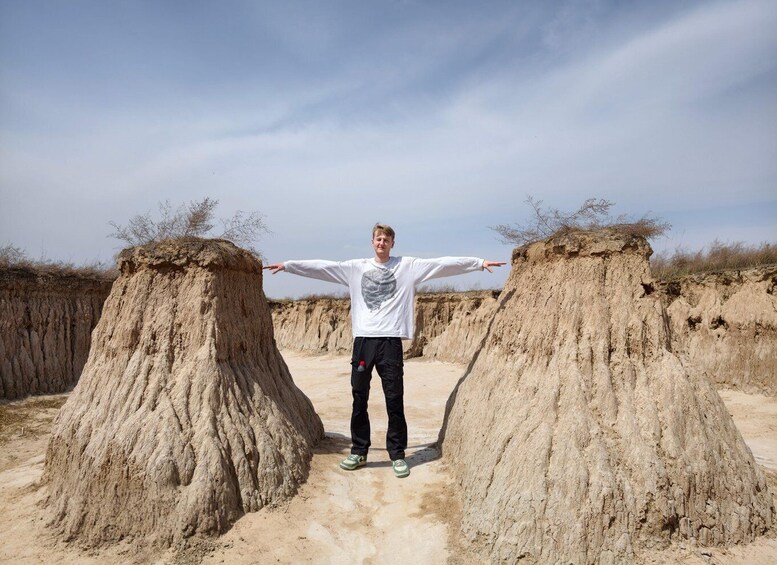 A person standing between two large sand mounds in a desert landscape. 3