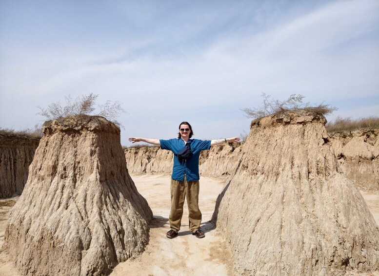 A person standing between two large sand mounds in a desert landscape. 2