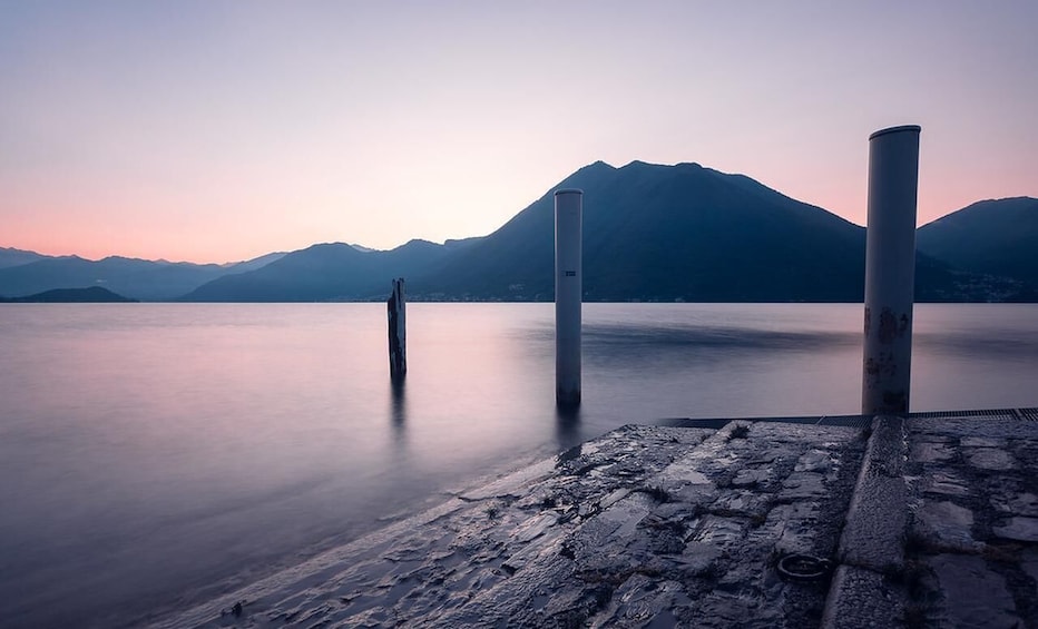 Un lago tranquilo con montañas al fondo y un muelle de piedra en primer plano. 5