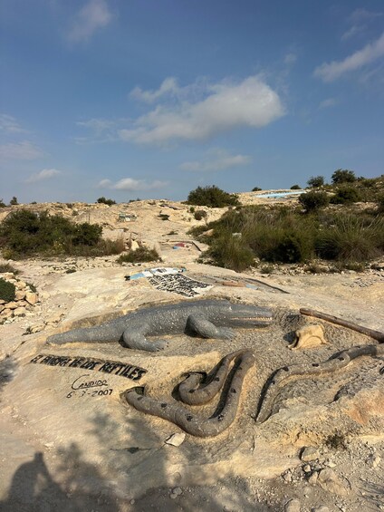 A large snake sculpture on a rocky terrain with sparse vegetation and a clear sky. 3