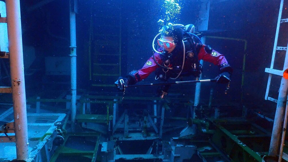 A diver in a red suit with a helmet and oxygen tank, surrounded by industrial structures and pipes. 2