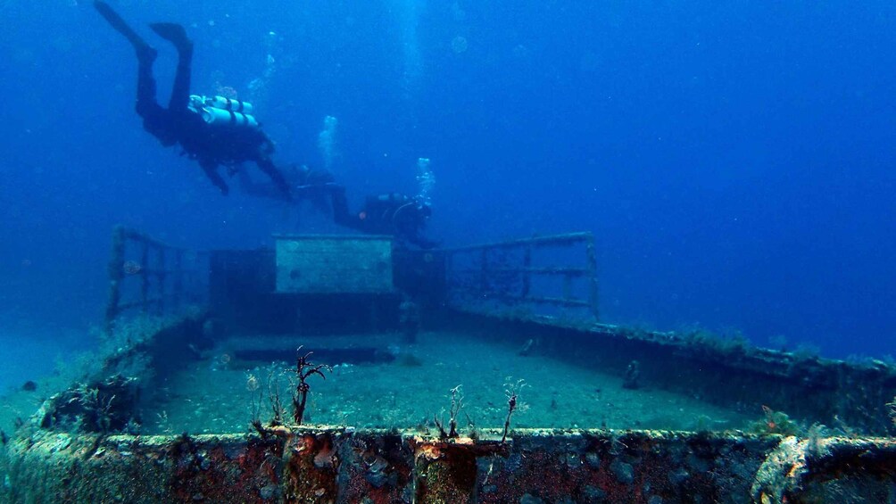 A diver exploring an underwater shipwreck with visible rust and marine growth. 4
