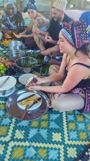 People sitting on a patterned mat, preparing food with vegetables and cooking utensils. 2
