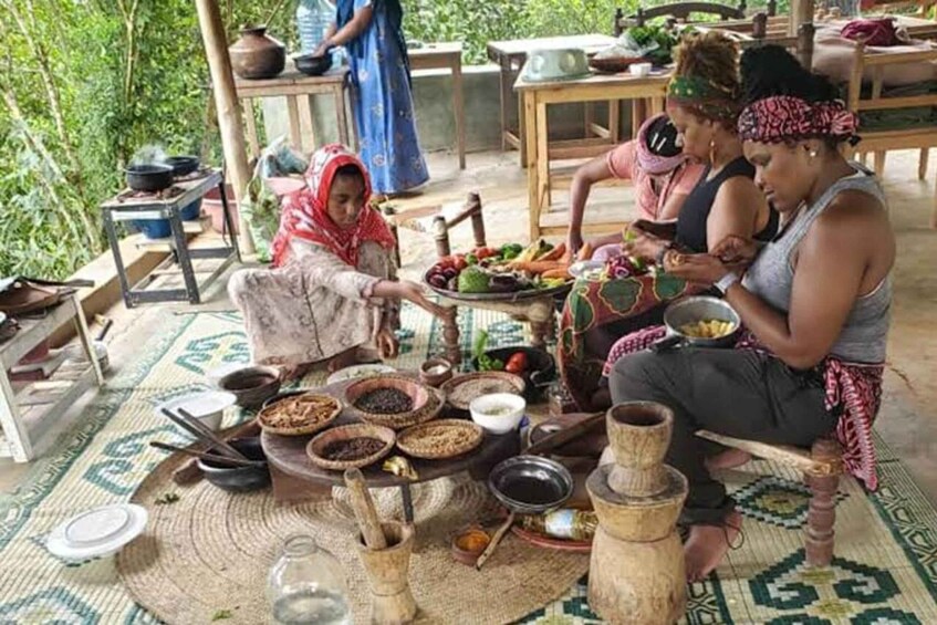 A group of people engaged in a traditional meal preparation outdoors, surrounded by various cooking utensils and ingredients. 4