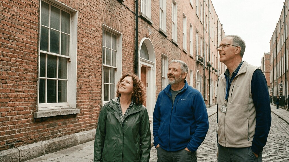 Three people standing on a cobblestone street in front of a brick building with arched windows. 4