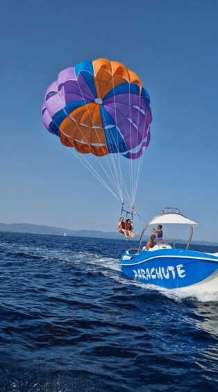 A parasailing activity with a colorful parachute above a blue boat named 'PARACHUTE' on the water. 1