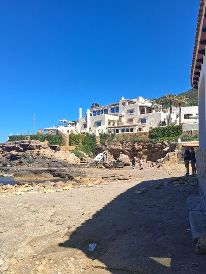 A coastal area with rocky terrain, a white building with multiple windows, and a clear blue sky. 2