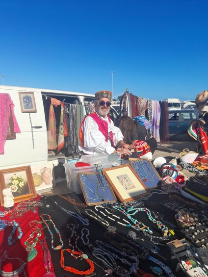 A vendor at a market stall with various jewelry and textiles on display. 3