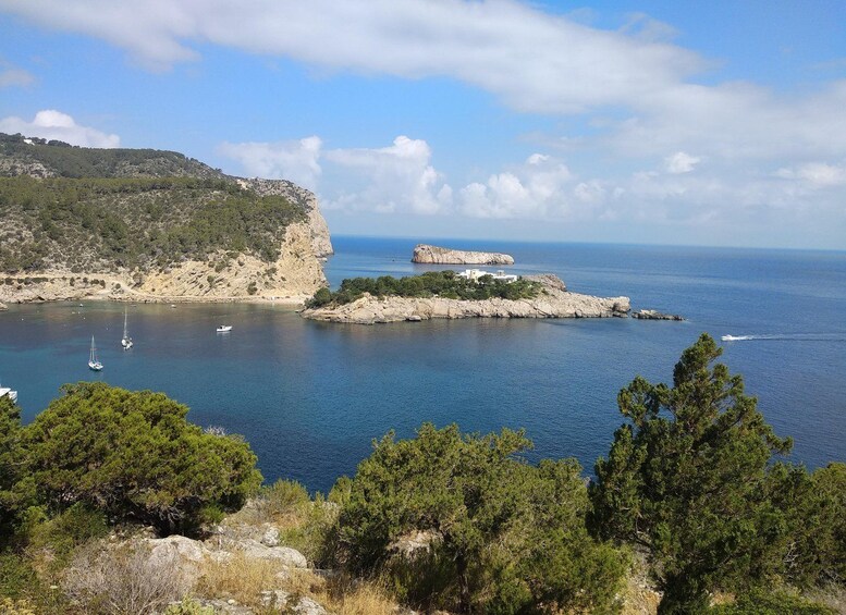 A coastal landscape with rocky cliffs, a small island with buildings, and boats in the water. 1