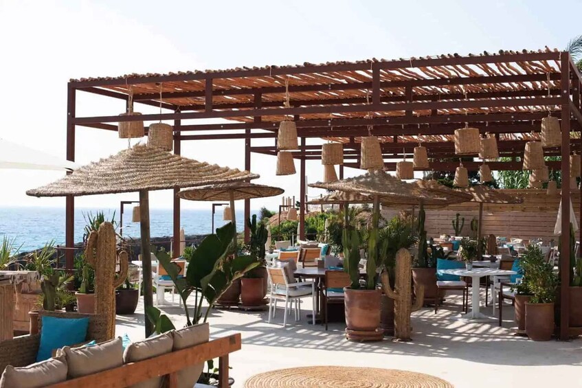 An outdoor seating area with tables and chairs, surrounded by potted plants and a wooden pergola with hanging lights. 4