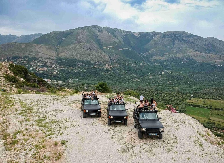 Three off-road vehicles parked on a gravel path with a mountainous landscape in the background. 1