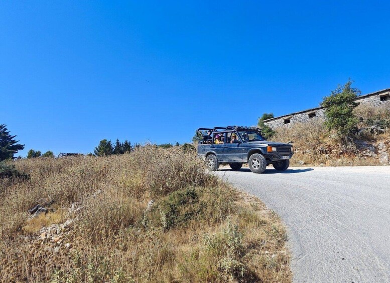 A blue off-road vehicle on a rural road with dry vegetation and a stone building in the background. 3