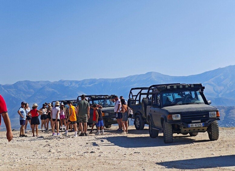 A group of people standing on a dirt path with mountains in the background and two off-road vehicles parked nearby. 2