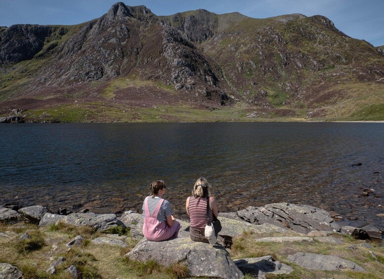 Two people sitting on rocks by a lake with mountains in the background. 5