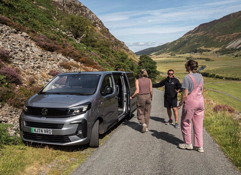 A silver van parked on a rural road with a mountainous landscape in the background. 2