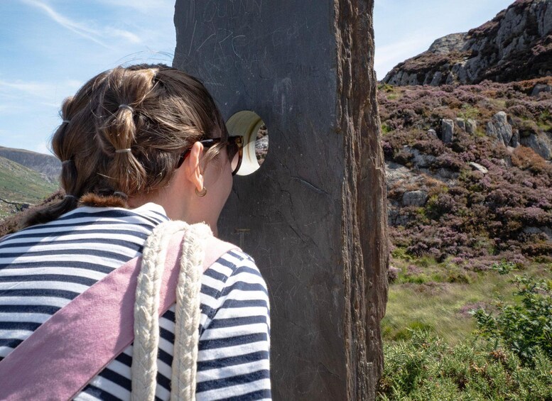 A person with a ponytail wearing a striped shirt and a pink scarf, looking at a large rock with inscriptions. 4