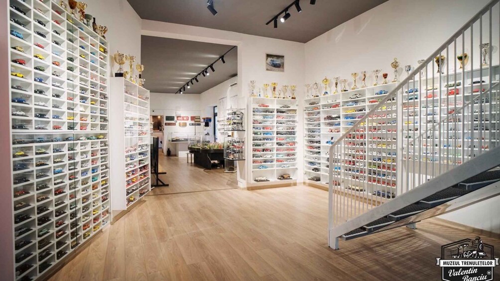 A showroom with multiple rows of model cars and trophies on shelves. 3