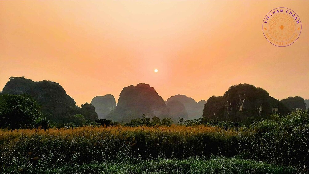 A sunset over a mountainous landscape with a field in the foreground. 1