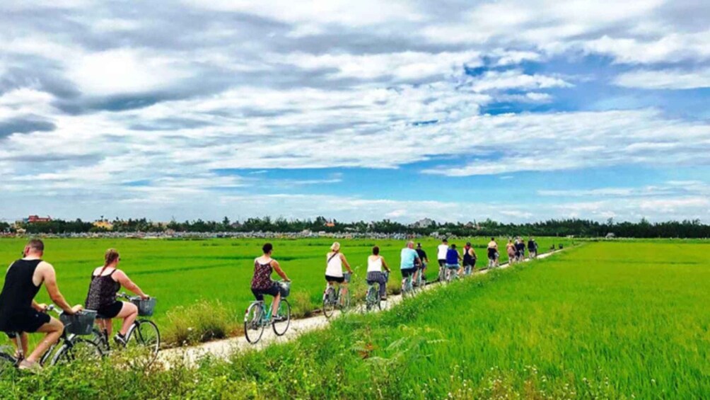 A group of cyclists on a path through a green field with a cloudy sky. 2