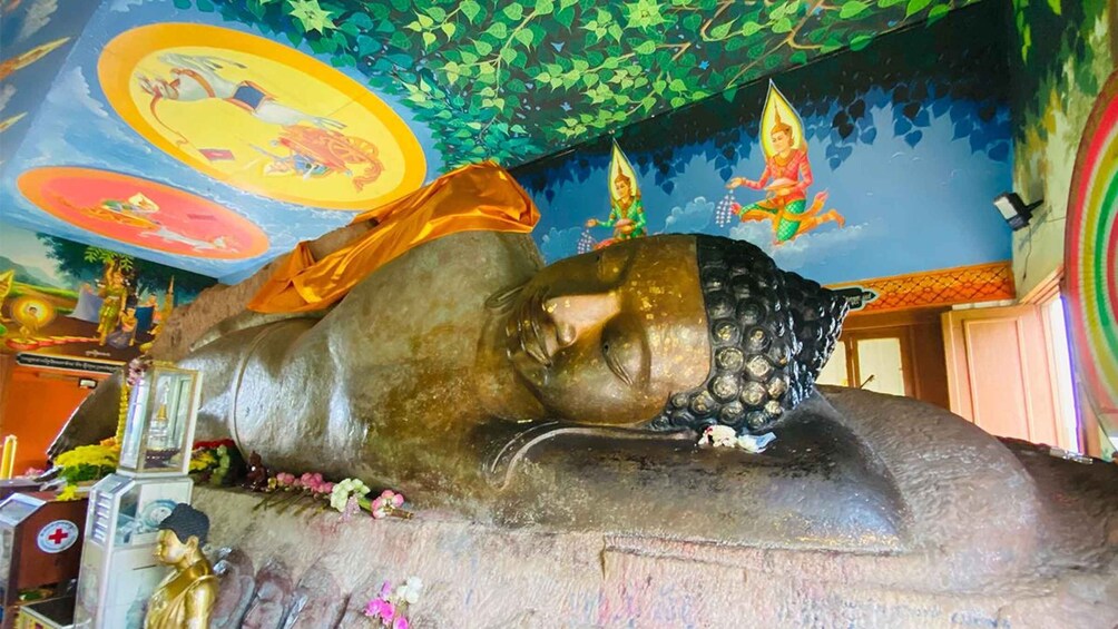 A large reclining Buddha statue with intricate carvings, surrounded by colorful murals and floral decorations. 3