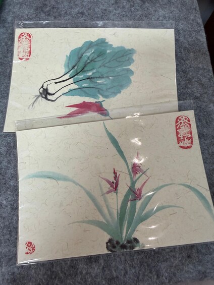 Two pieces of artwork with traditional Asian motifs, one depicting a bird and the other featuring plants. 2