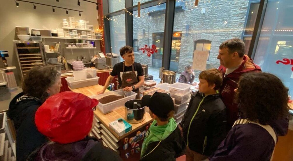 A group of people in a modern kitchen setting with large windows and a stone wall visible outside. 4