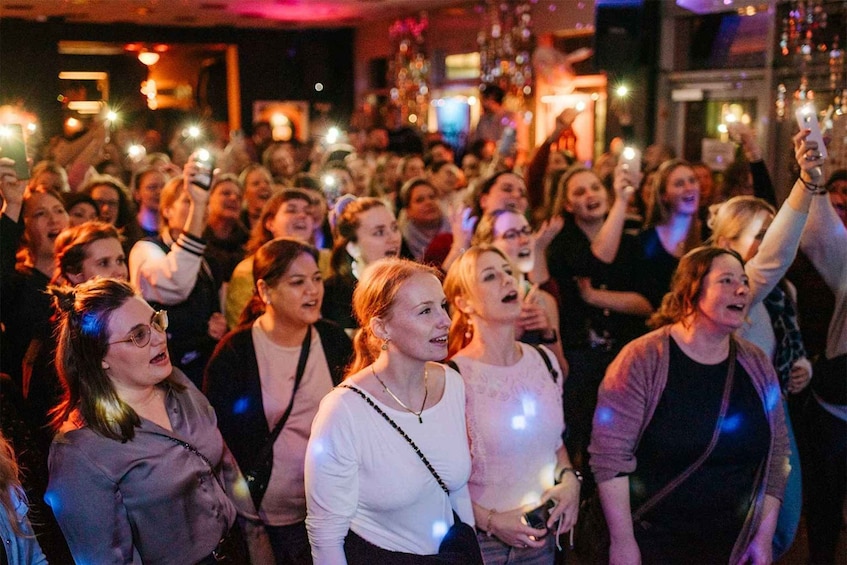 A crowded indoor event with people holding up their phones, likely taking photos or videos. 5