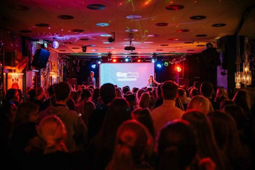 A crowded indoor event with a stage and a screen displaying the word 'elong.' 4