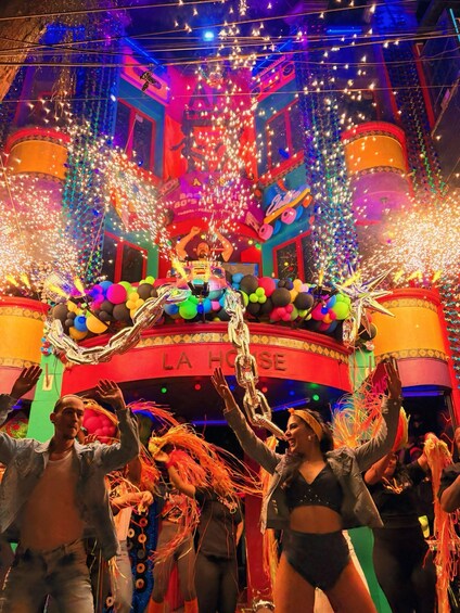 A vibrant celebration with people dancing, colorful balloons, and a decorated stage with the text 'LA HOUSE'. 1