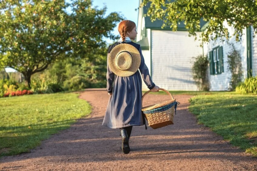 A person walking on a dirt path with a basket, wearing a hat, and a long dress. 2