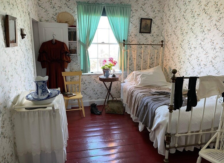 A bedroom with floral wallpaper, a wooden chair, a bedside table with a vase, a bed with white linens, and a window with curtains. 5