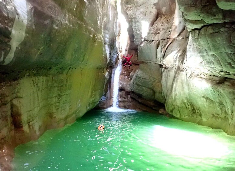 A person swimming in a green pool with a waterfall in a cave. 4