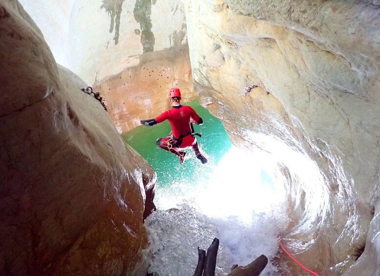 A person in a red suit rappelling down a rocky, narrow passage. 1