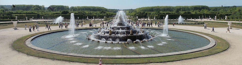 A large circular fountain with multiple water jets, surrounded by a well-maintained garden and walking paths. 1