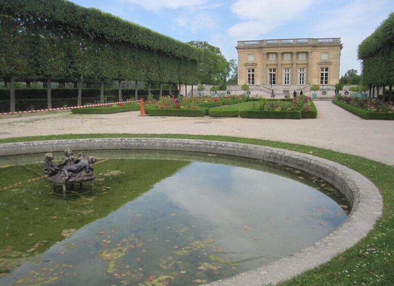 A classical building with a formal garden, including a circular pond with statues and neatly trimmed hedges. 3