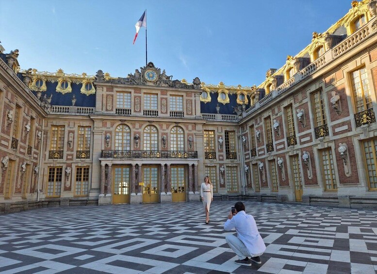 A grand building with a checkered floor, a flag, and a person taking a photo. 1