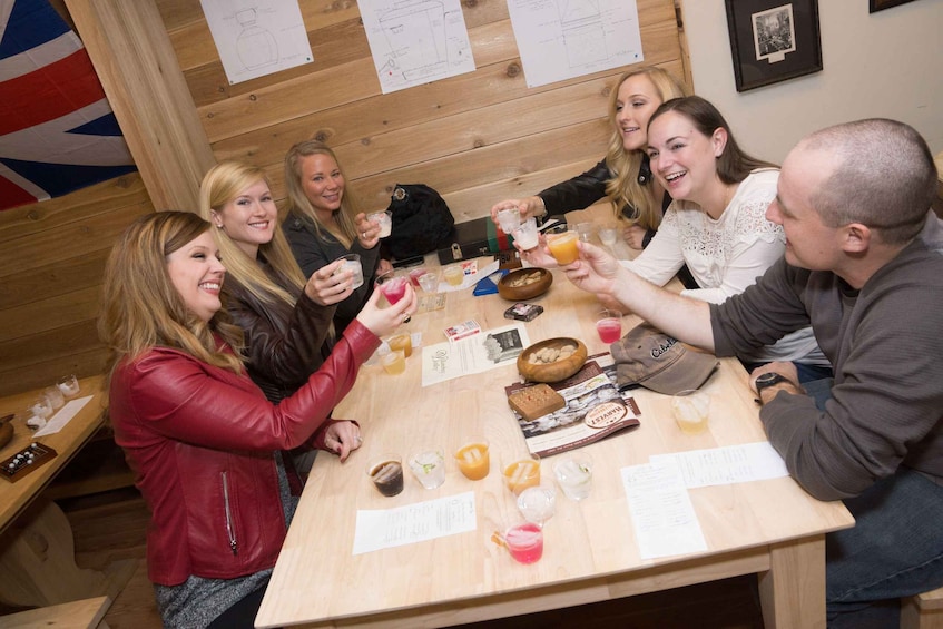 A group of people toasting with drinks around a wooden table with food and papers. 2