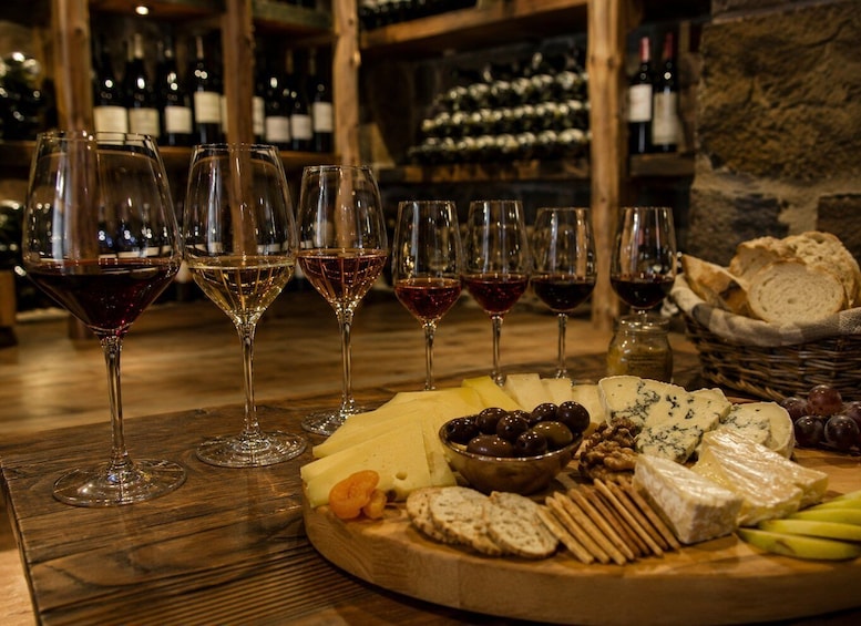 A wooden table with a cheese and wine tasting setup, including various cheeses, olives, nuts, and bread. 1