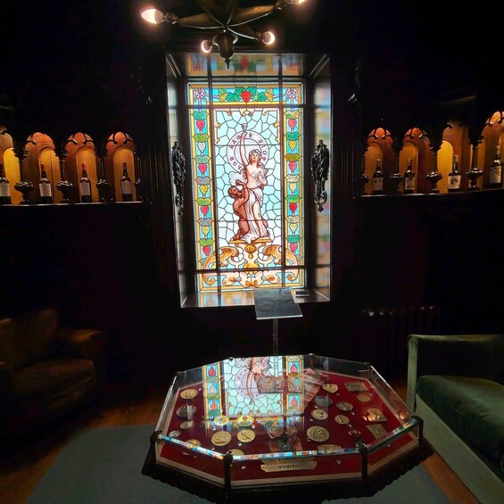 A stained glass window with a central figure, surrounded by bottles on shelves, and a display case with coins labeled 'PORTO'. 2