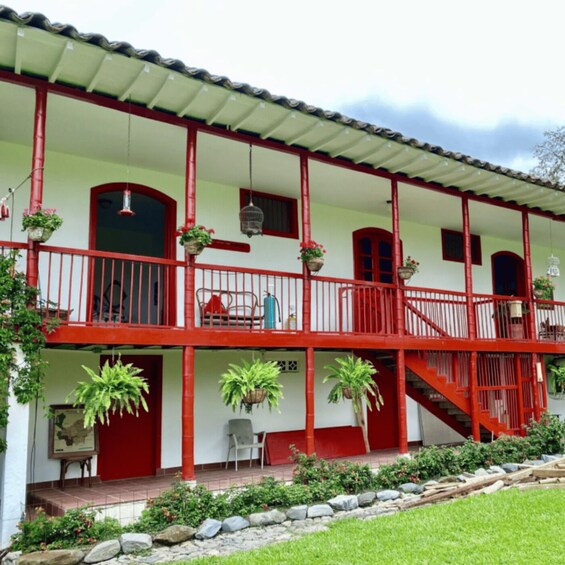 A two-story building with red railings and columns, a balcony, and hanging plants. 1