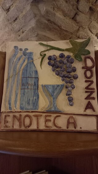 A ceramic sign with 'DONZA' and 'ENOTECA' text, a bottle, a glass, and grapes. 5