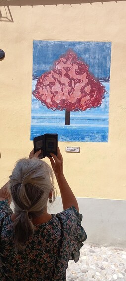 A person taking a photo of a painting of a tree on a wall. 4