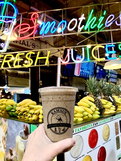 A hand holding a cup with a straw, a neon sign reading 'Smoothies & Fresh Juices,' and a display of bananas and pineapples. 3