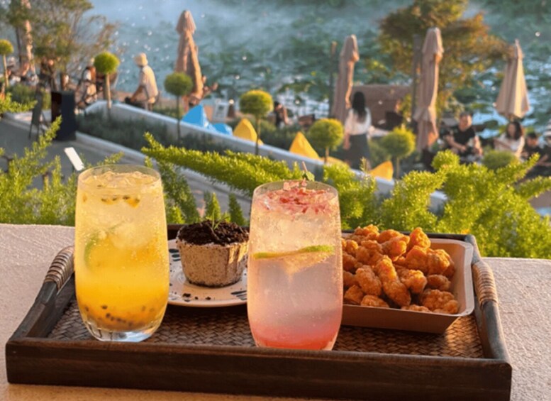 A tray with two drinks, a dessert, and fried food, set against a scenic outdoor backdrop. 4
