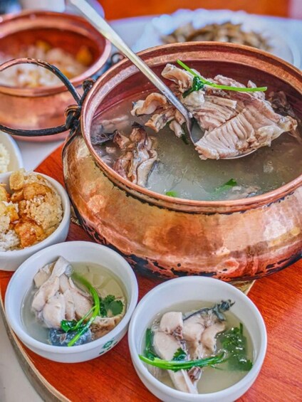 A copper pot with a ladle, surrounded by bowls of soup and rice. 5