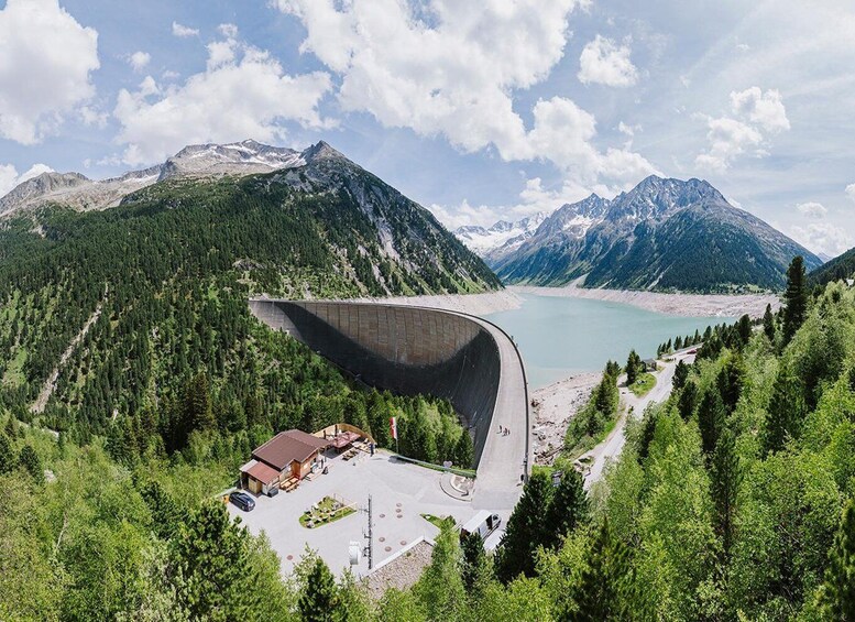 A large dam with a curved structure, surrounded by forested mountains and a lake. 2